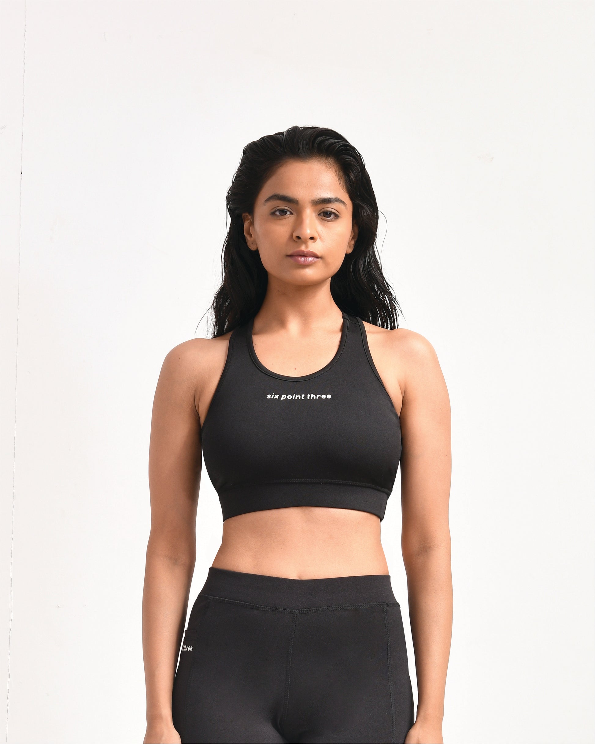 Woman wearing black high-compression sports bra with Six Point Three logo, ideal for intense workouts, featuring racerback design and moisture-wicking fabric for maximum support and comfort.
