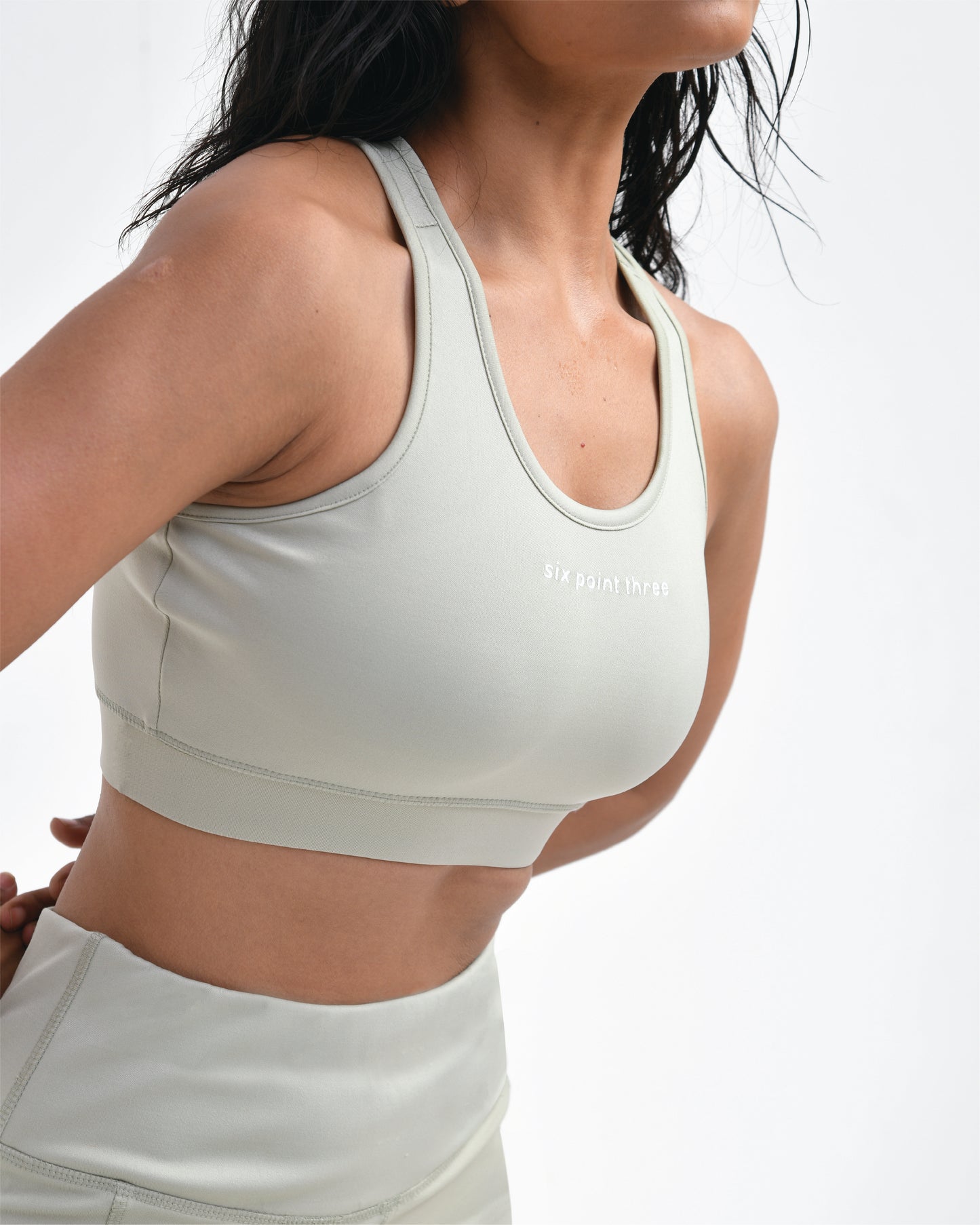 Woman wearing a light sage sports bra by Six Point Three, leaning forward to show good compression, designed for high-impact workouts and seamless support, perfect as a sports bra for the gym.